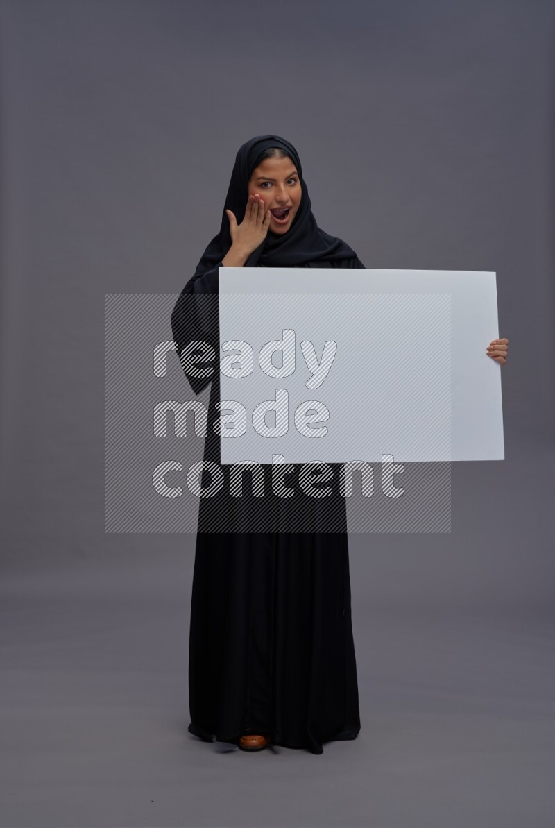 Saudi woman wearing Abaya standing holding white board on gray background
