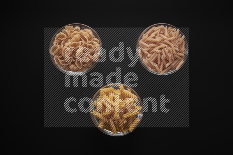Different pasta types in glass bowls on black background