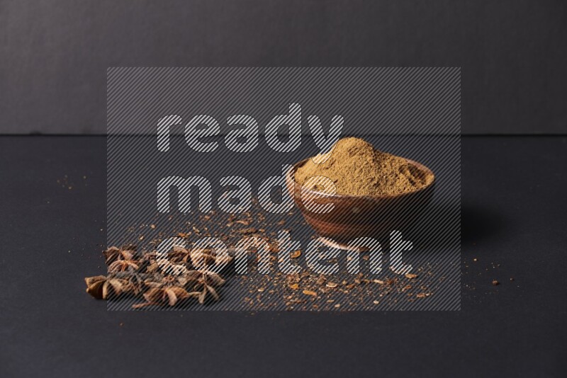 Star Anise powder in a wooden bowl with star anise beside it on a black background