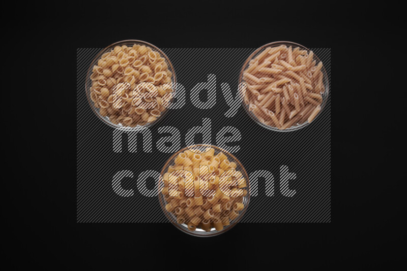 Different pasta types in glass bowls on black background