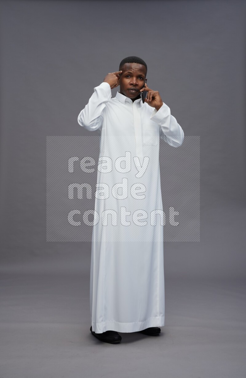 Saudi man wearing thob standing talking on phone on gray background