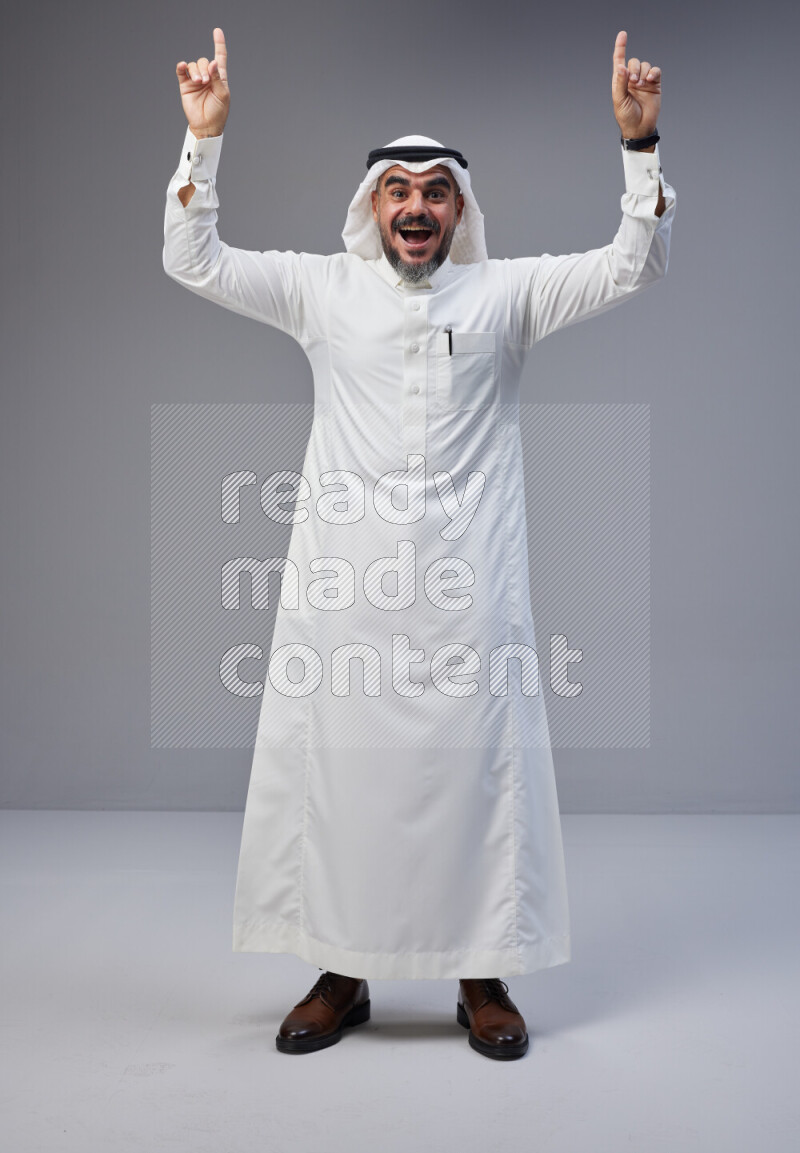 Saudi man Wearing Thob and white Shomag standing interacting with the camera on Gray background