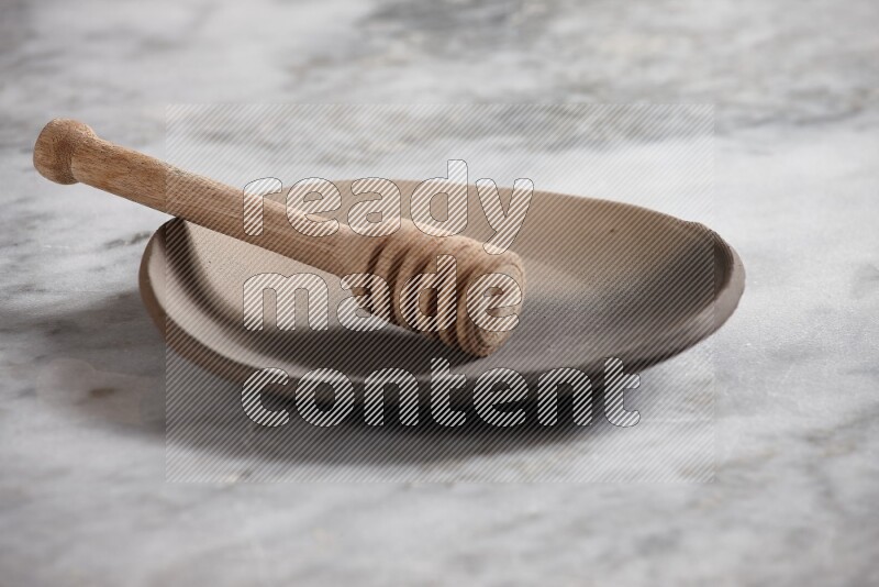 Multicolored pottery plate with wooden honey dipper in it on grey marble background