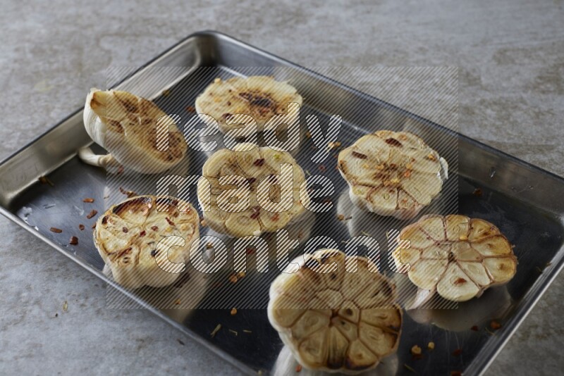 half's roasted garlic in a stainless tray on a grey textured countertop