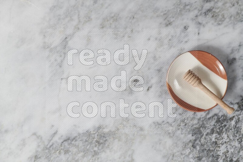 طبق فخاري متعدد الألوان مع ملعقة عسل خشبية بداخله على خلفية من الرخام الرمادي