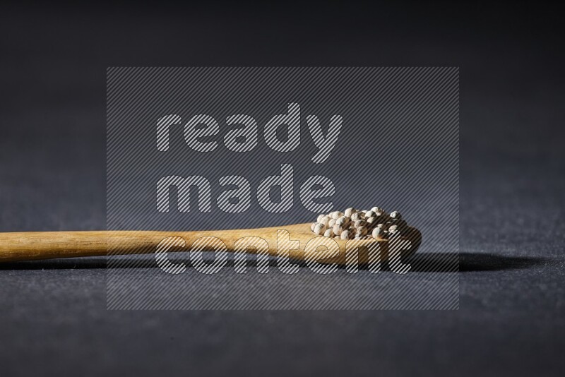 ملعقة خشبية مملوءة بحبات الفلفل الأبيض على أرضية سوداء