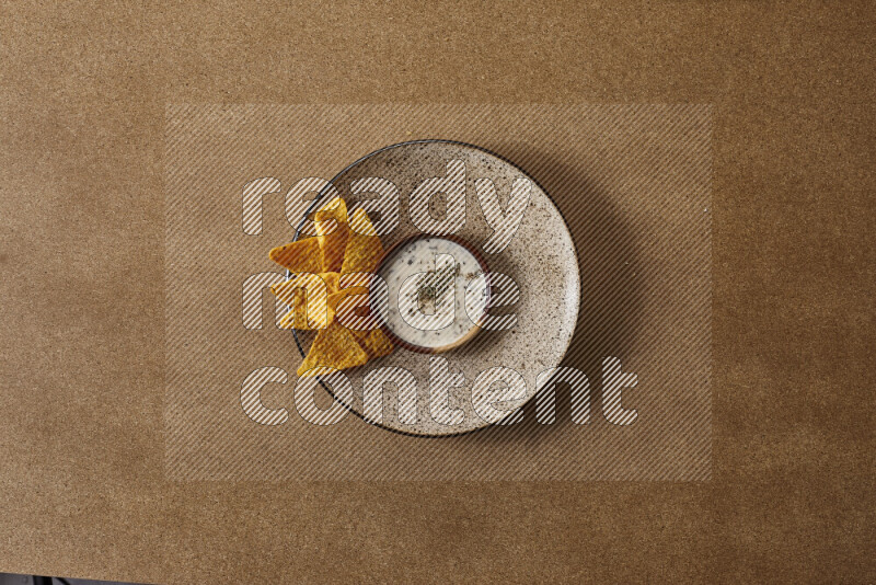 Assorted snacks on a pottery plate with a dipping on brown background