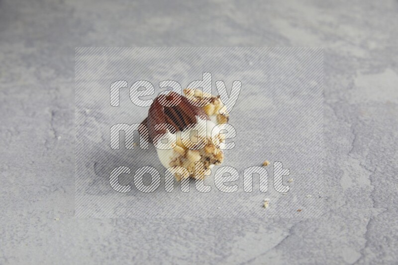 Two pecan stuffed date covered with white chocolate and chopped walnuts on alight grey background