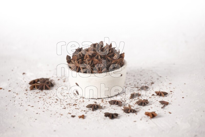 Star Anise in a white bowl and more of it sprinkled on white background