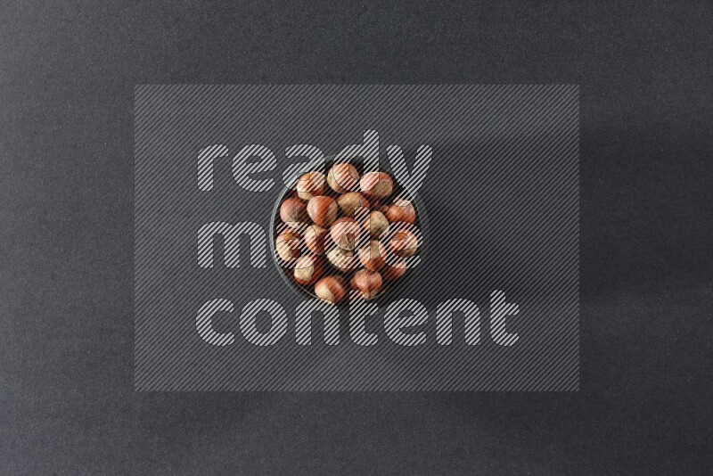 A black pottery bowl full of hazelnuts on a black background in different angles