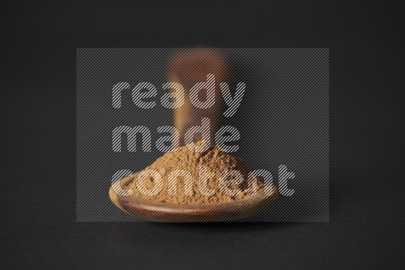Cinnamon powder in a spoon ladle on black background