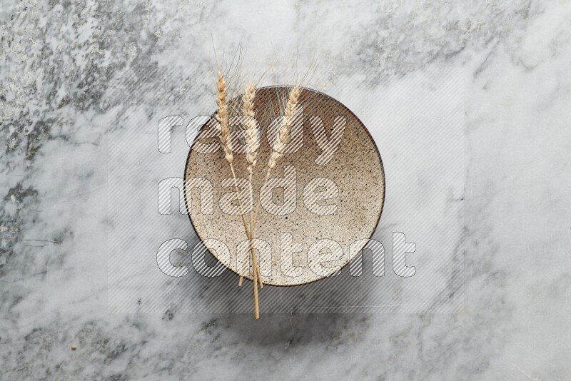 Wheat stalks on multicolored pottery plate on grey marble background