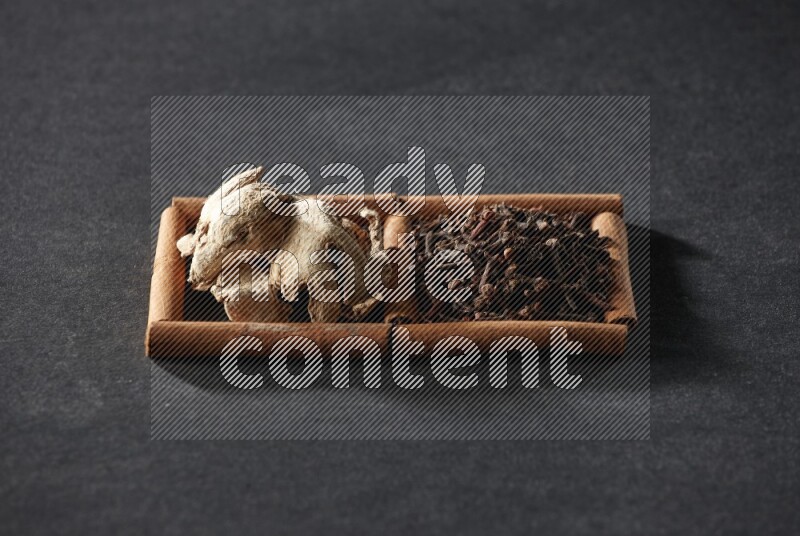 2 squares of cinnamon sticks full of cloves and dried ginger on black flooring