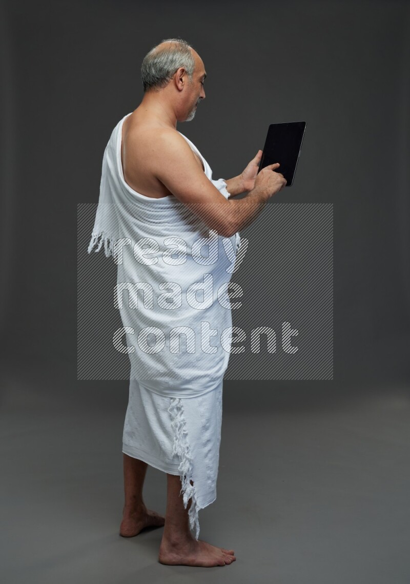 A man wearing Ehram Standing working on tablet on gray background