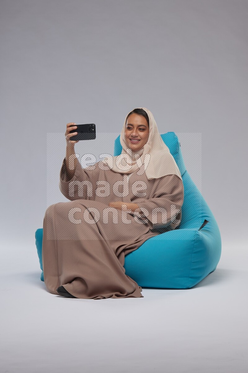 A Saudi woman sitting on a blue beanbag and taking selfie