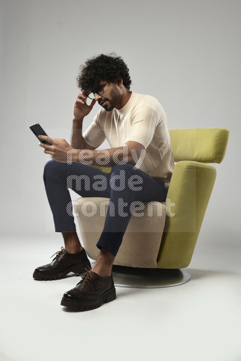 A man wearing casual sitting on a chair browsing on the phone on white background