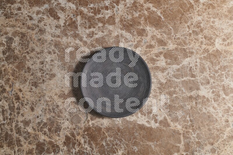 A circular black pottery plate on beige marble background