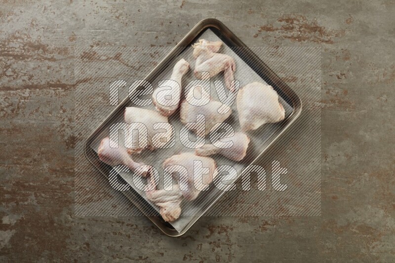 Mixed fresh chicken pieces in an oven tray on a textured rustic background