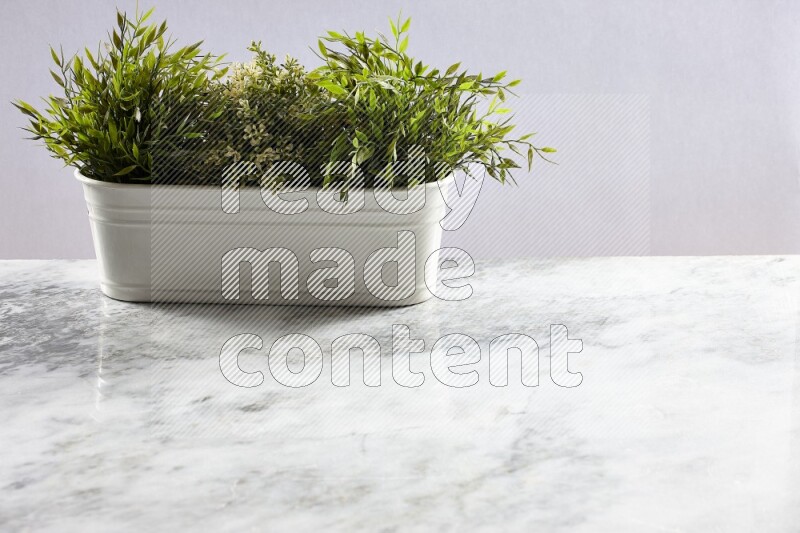 Multiple green artificial plants in white pot on grey marble background