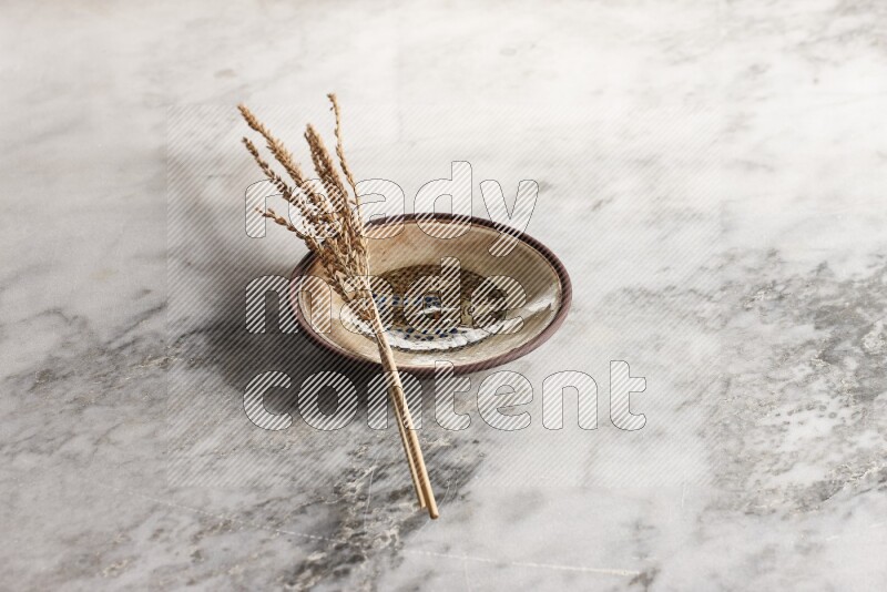 Wheat stalks on decorative pottery plate on grey marble background