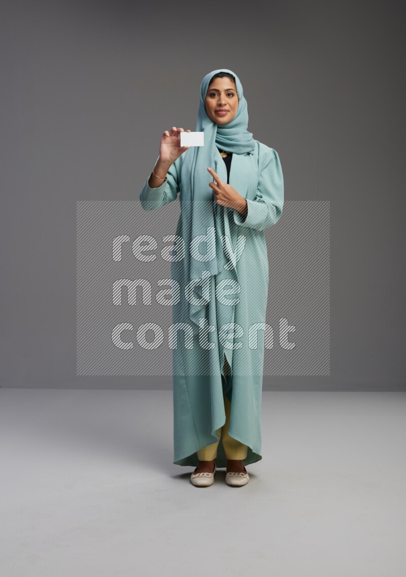 Saudi Woman wearing Abaya standing holding ATM card on Gray background