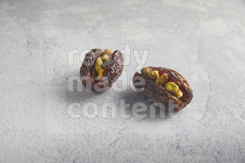 two pistachio stuffed madjoul date on a light grey background
