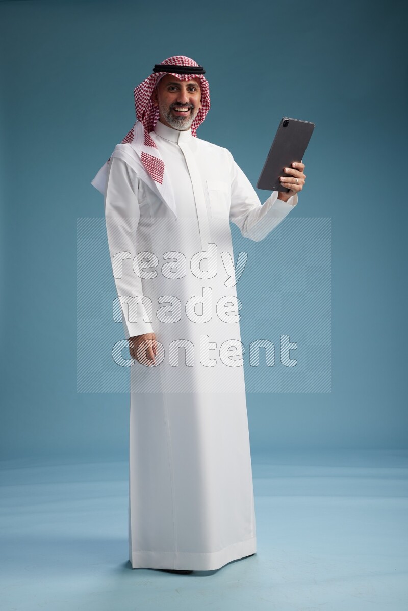 Saudi man wearing thob and shomagh with tablet on Blue background