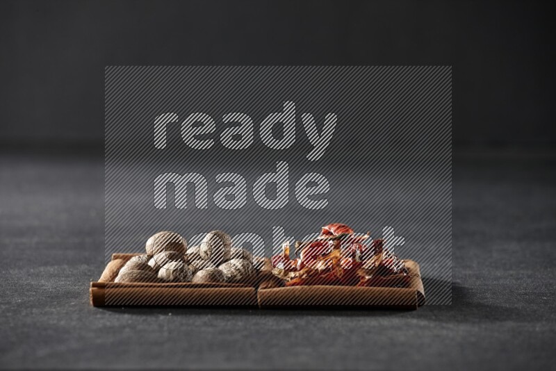 2 squares of cinnamon sticks full of nutmegs and dried red chilis on black flooring