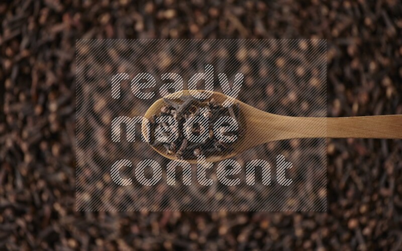 A wooden spoon full of cloves on cloves background and black flooring
