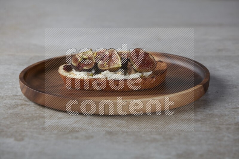 figs halves with cream cheese on toasted sourdough slice on a wooden board on textured grey background
