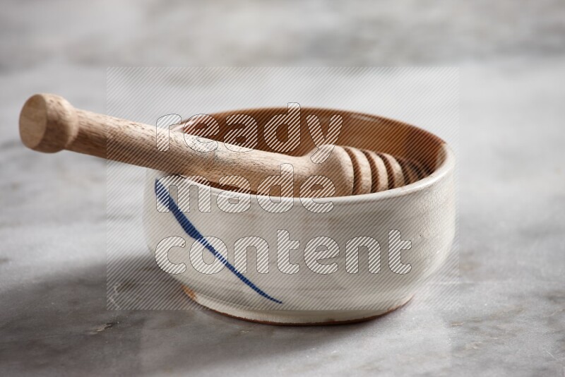 Multicolored pottery bowl with wooden honey dipper in it on grey marble background