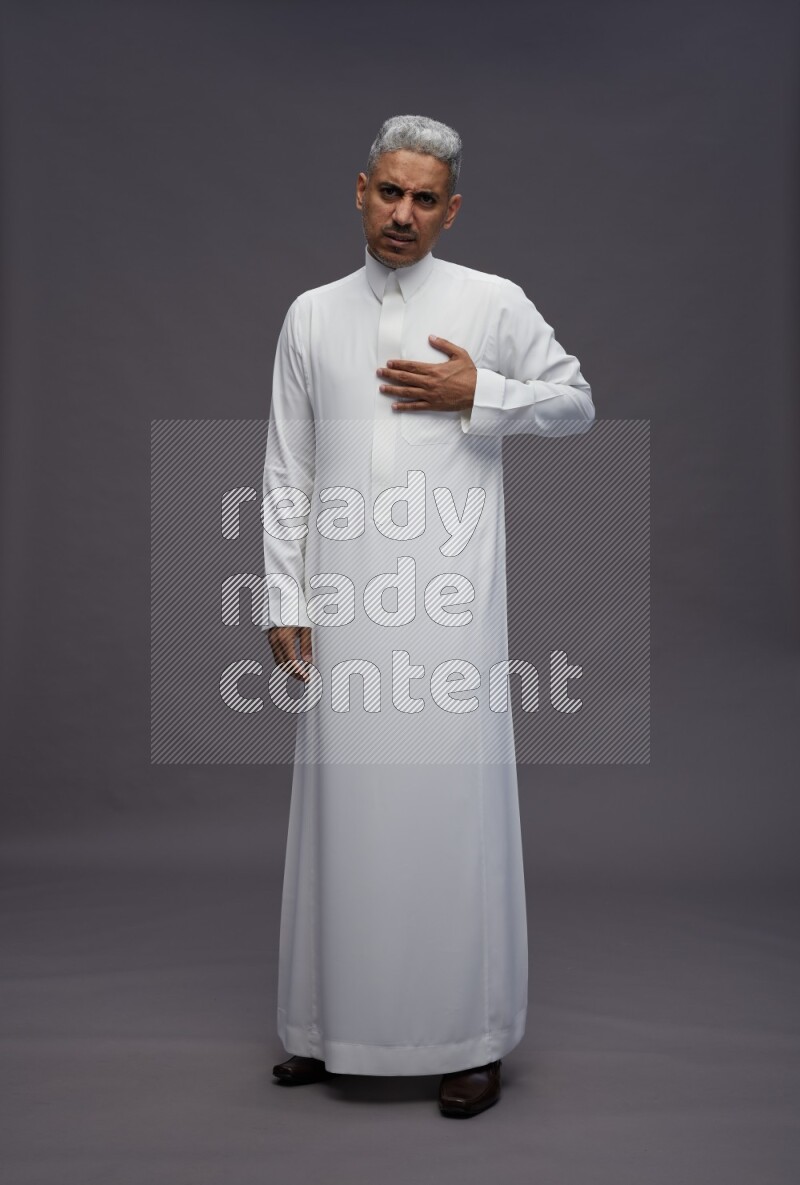 Saudi man wearing thob standing interacting with the camera on gray background