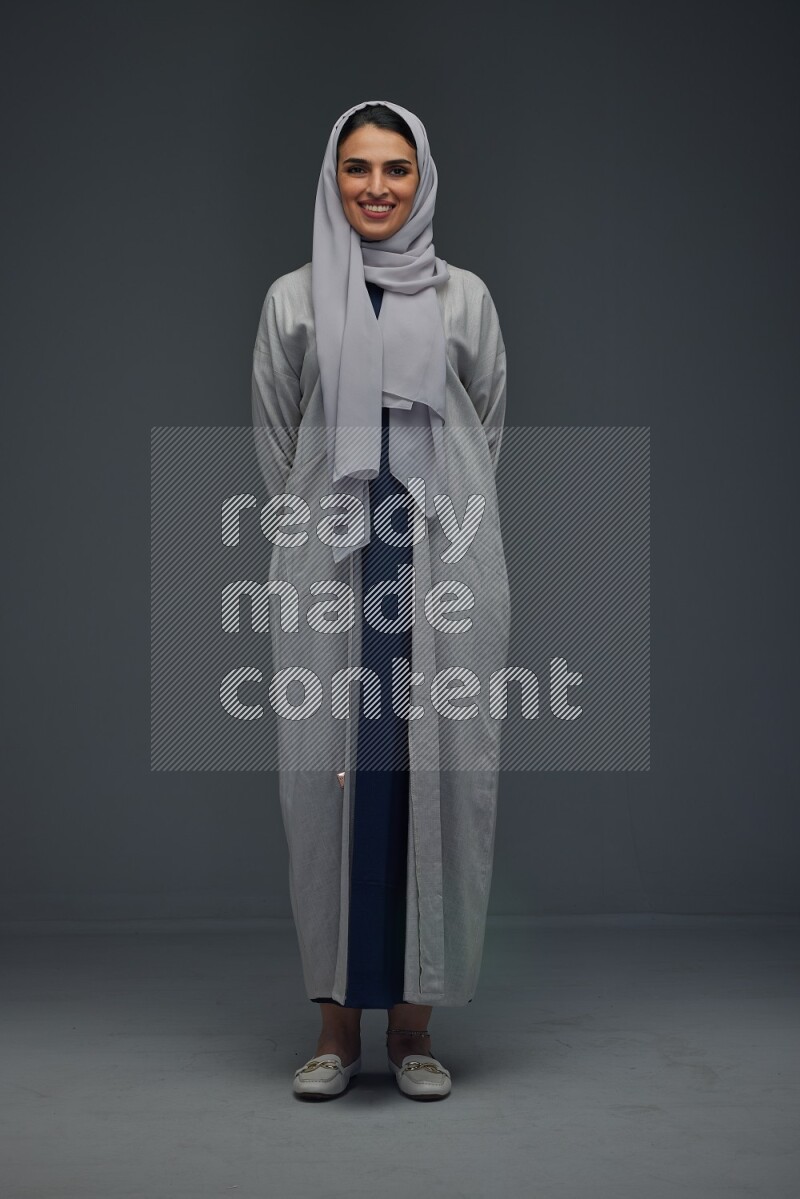 A Saudi woman wearing a light gray Abaya and head scarf standing and making multi poses eye level on a grey background