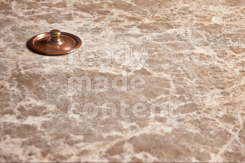 A small copper pot lid on beige marble background