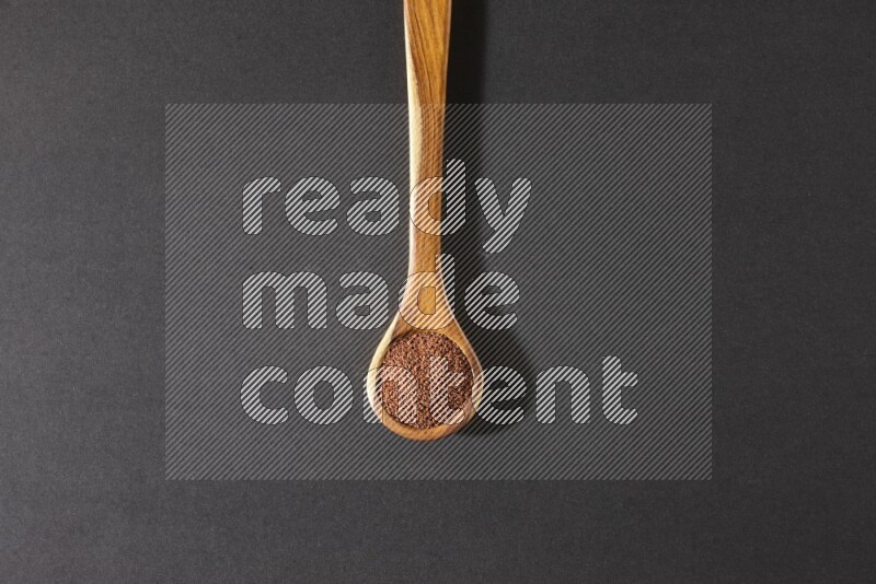 A wooden ladle full of garden cress seeds on a black flooring