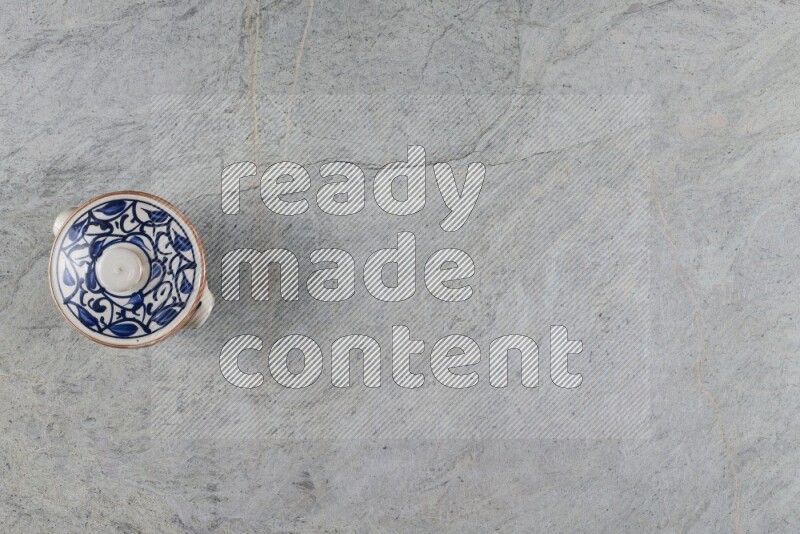 إناء فخاري متعدد الألوان مع غطائه على خلفية من الرخام الرمادي