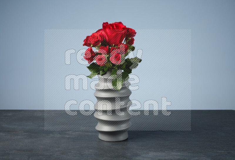An arrangement of vivid red roses in a grey spiral vase on black marble background