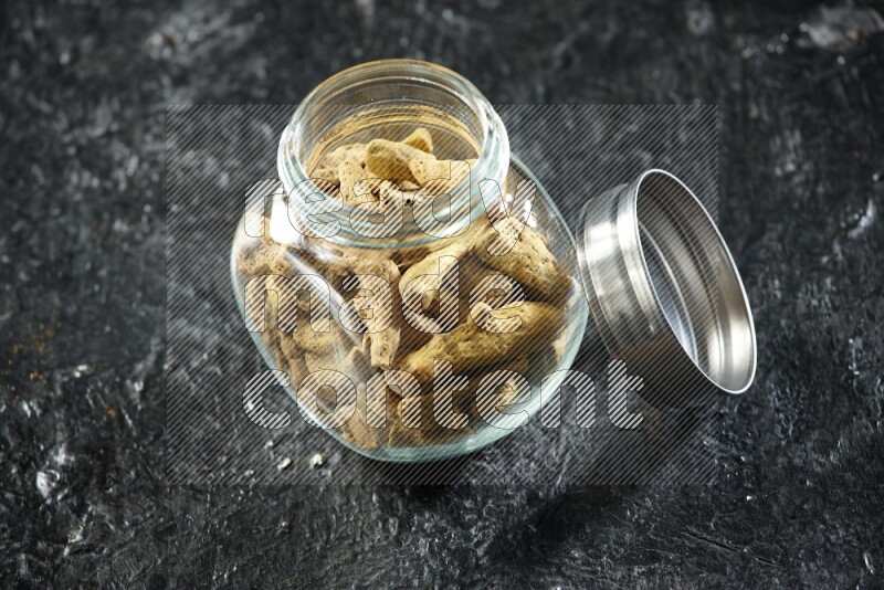 A glass spice jar full of dried turmeric whole fingers on a textured black flooring