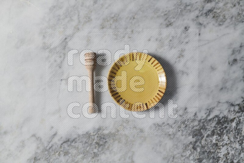 طبق فخاري متعدد الألوان مع ملعقة عسل خشبية بجانبه على خلفية رخام رمادي