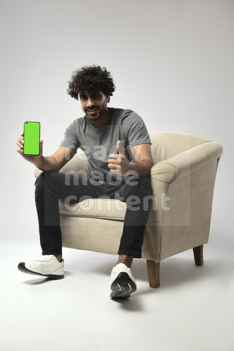 A man wearing casual sitting on a chair showing a phone screen on white background