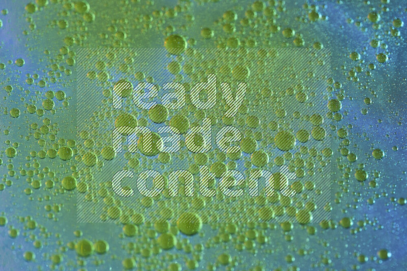 Close-ups of abstract yellow watercolor drops on oil Surface on blue background