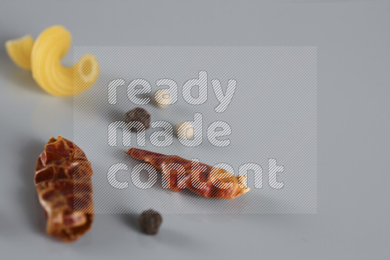 Raw pasta with different ingredients such as cherry tomatoes, garlic, onions, red chilis, black pepper, white pepper, bay laurel leaves, rosemary, cardamom and mushrooms on light blue background