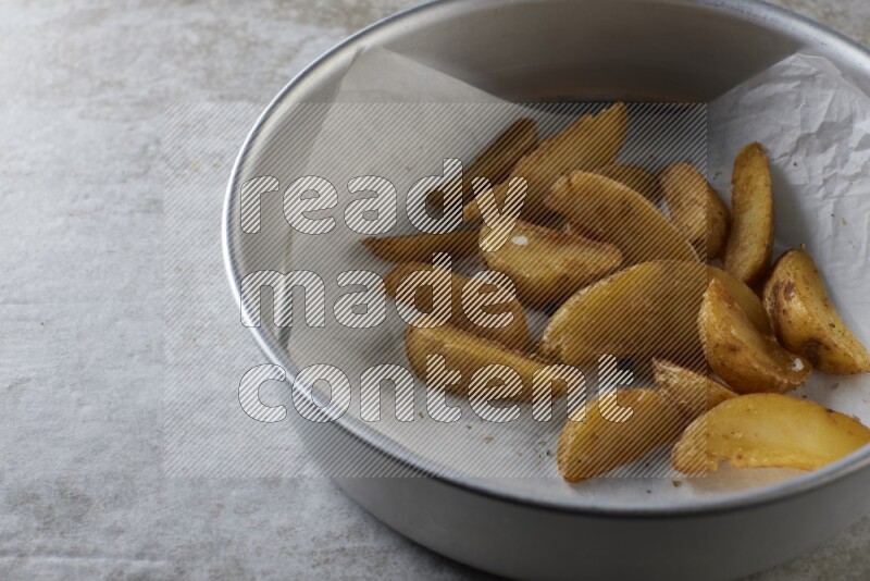 wedges potato on parchment paper in a stainless steel round tray on grey textured counter top