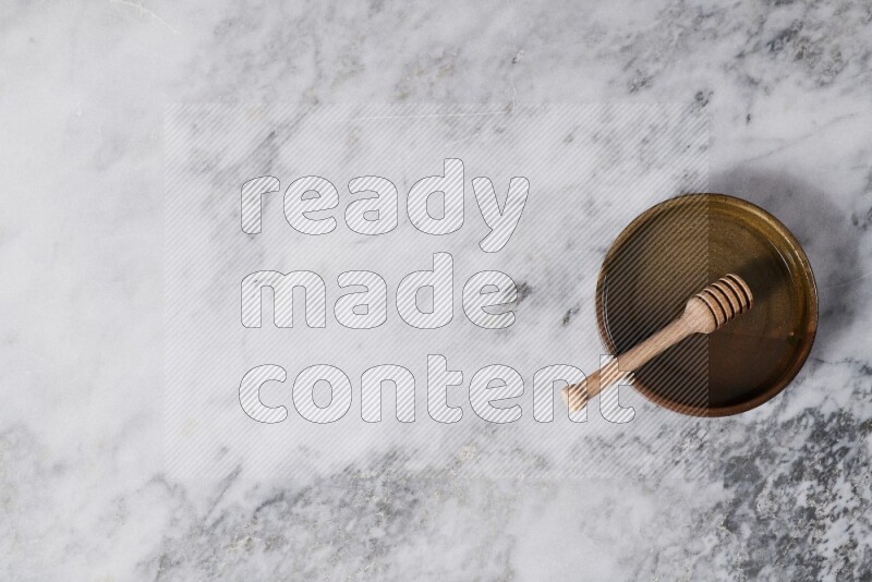 وعاء فرن فخاري متعدد الألوان مع ملعقة عسل خشبية بداخله على خلفية من الرخام الرمادي