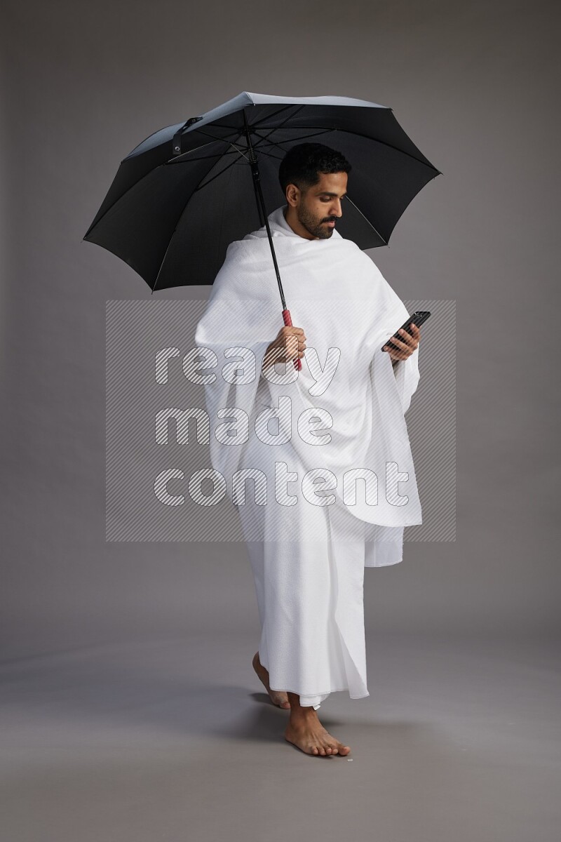 A man wearing Ehram Standing holding umbrella on gray background