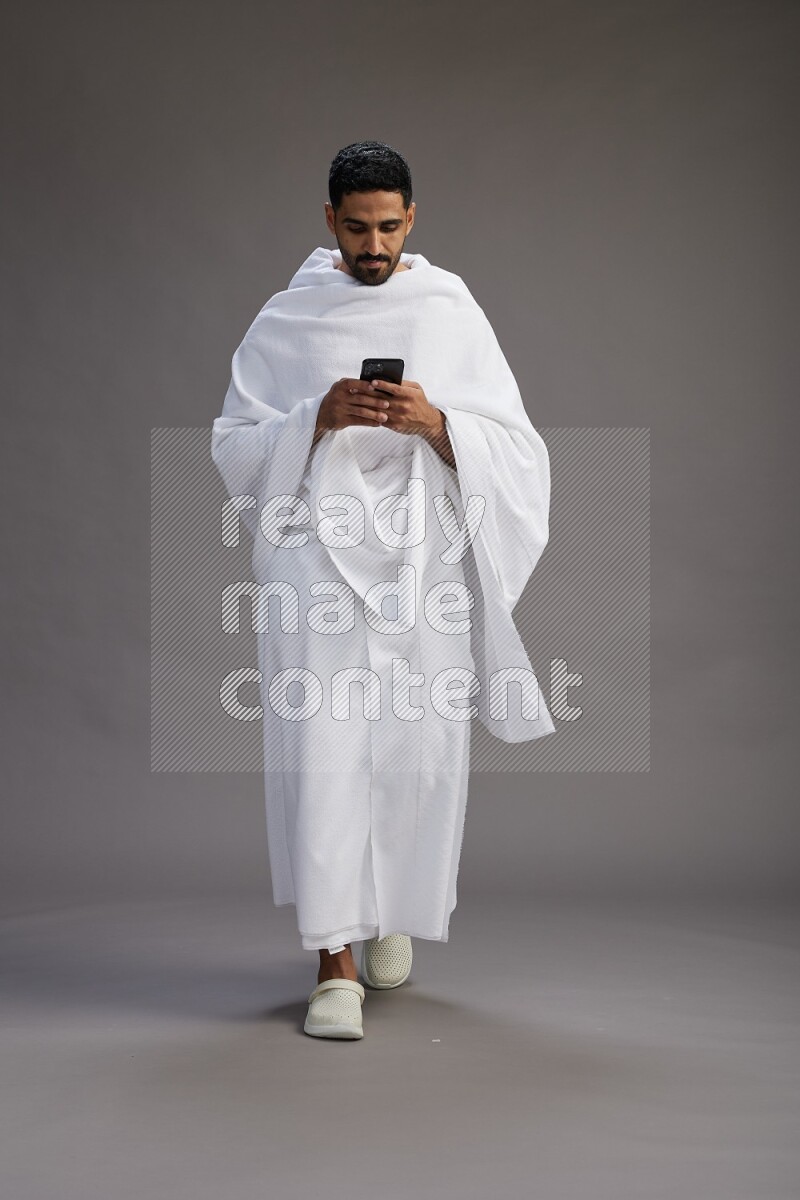 A man wearing Ehram Standing texting on phone on gray background