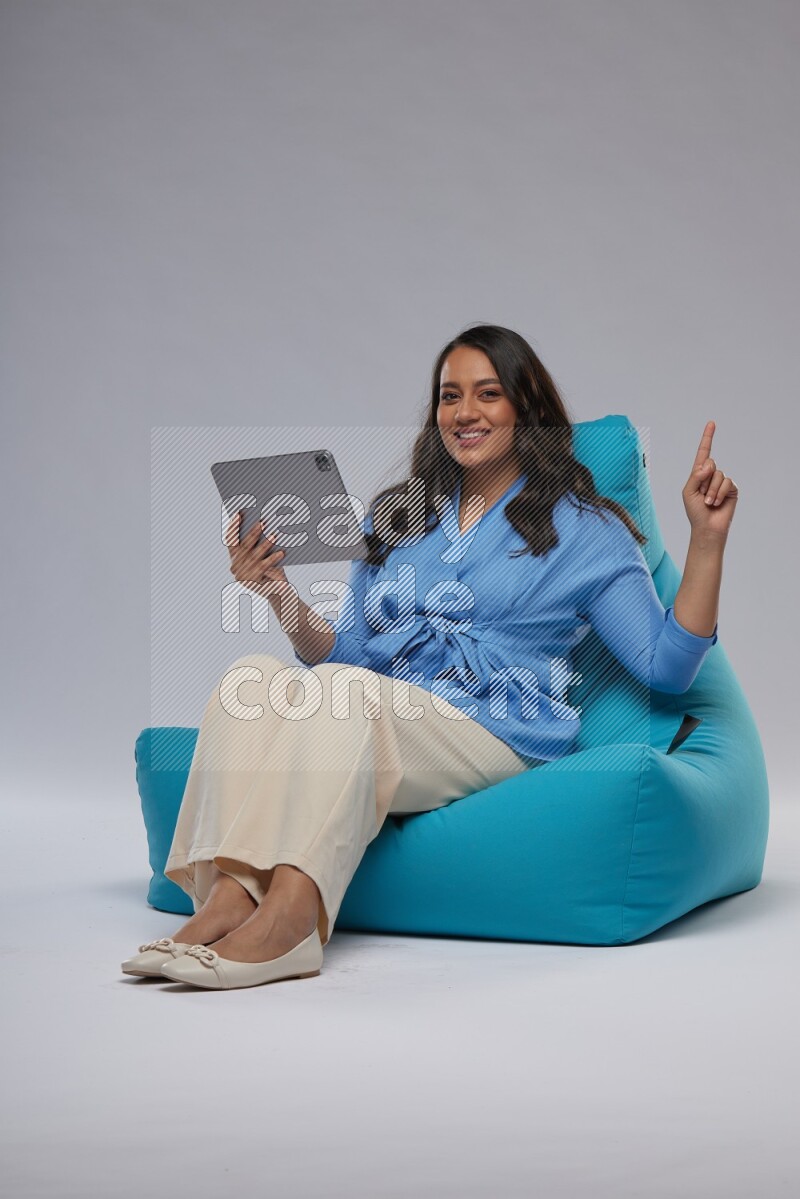 A woman sitting on a blue beanbag and working on tablet