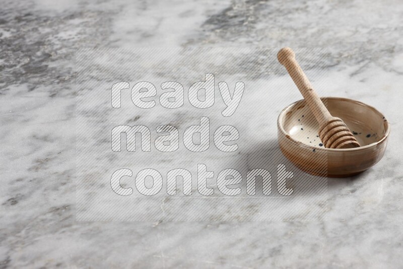 Multicolored pottery bowl with wooden honey dipper in it on grey marble background