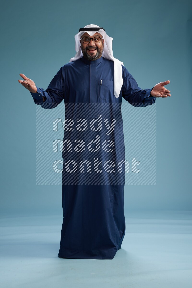 Saudi Man with shimag Standing Interacting with the camera on blue background