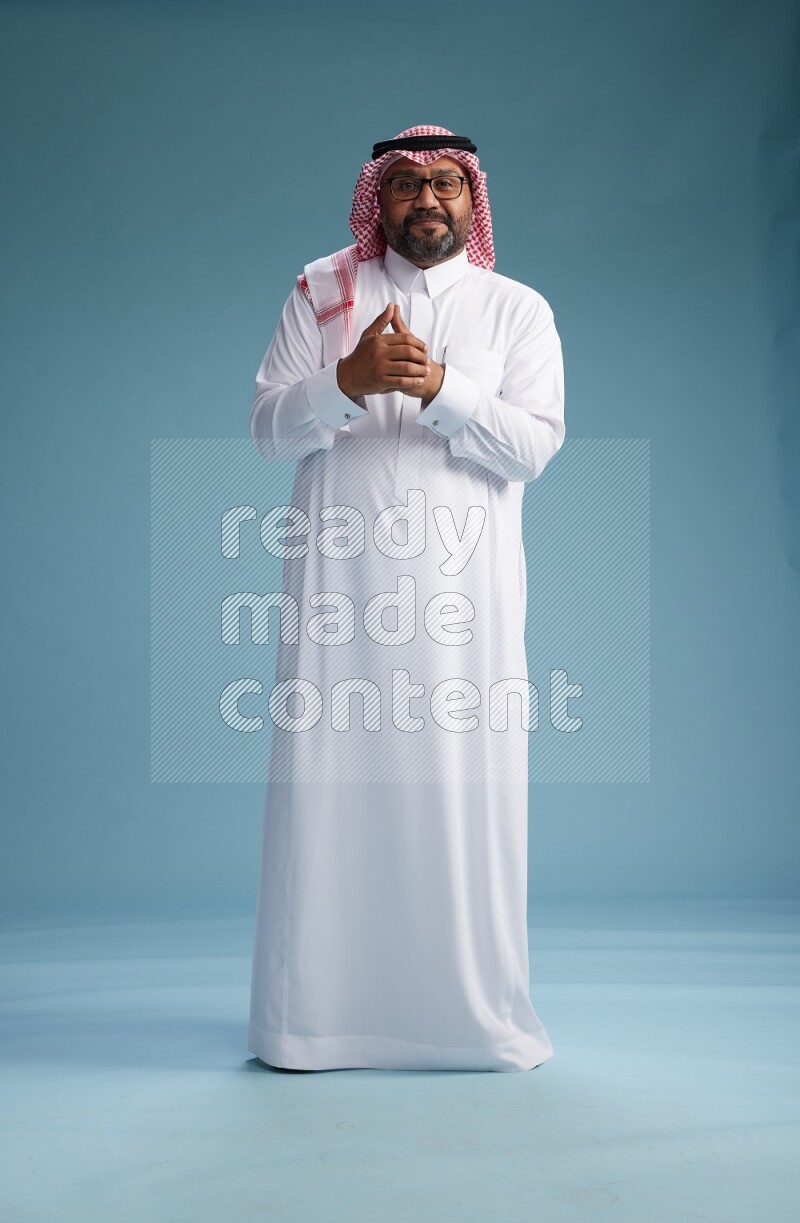 Saudi Man with shimag Standing Interacting with the camera on blue background